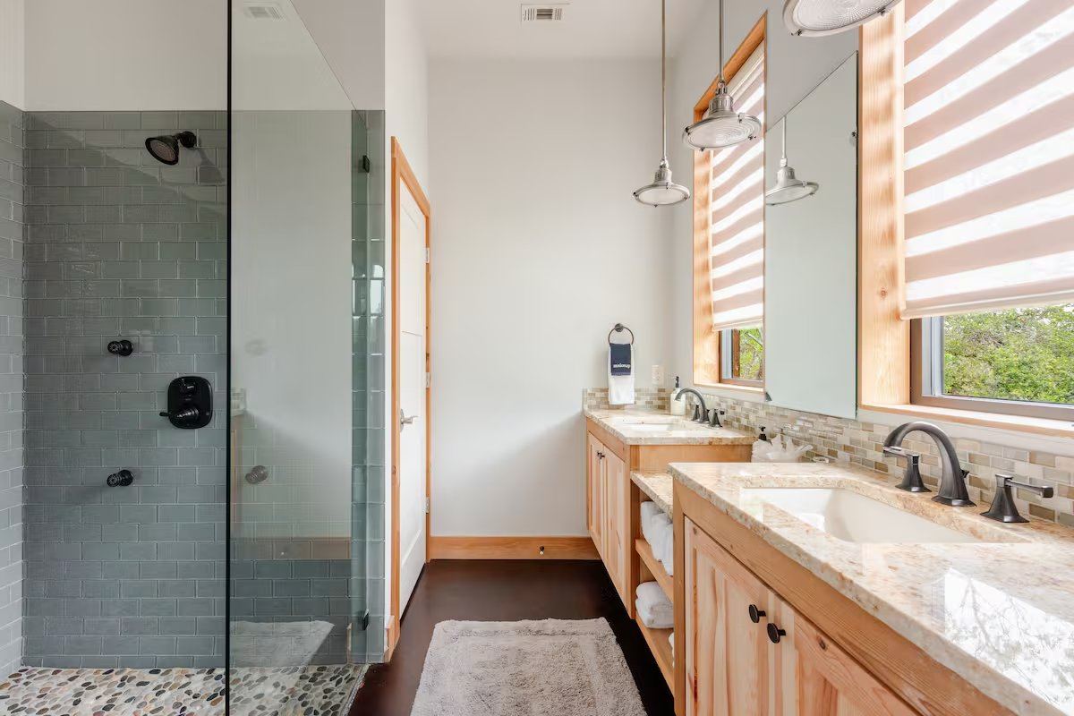 La Paz primary bathroom — double vanity with granite, glass walk-in shower, and natural light from large windows