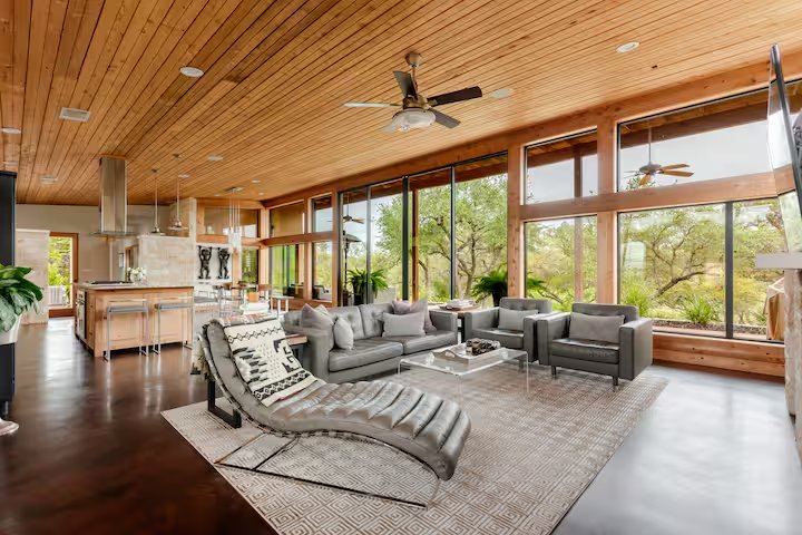 La Paz living room — wood ceiling, walls of glass, leather chaise, and an open kitchen beyond